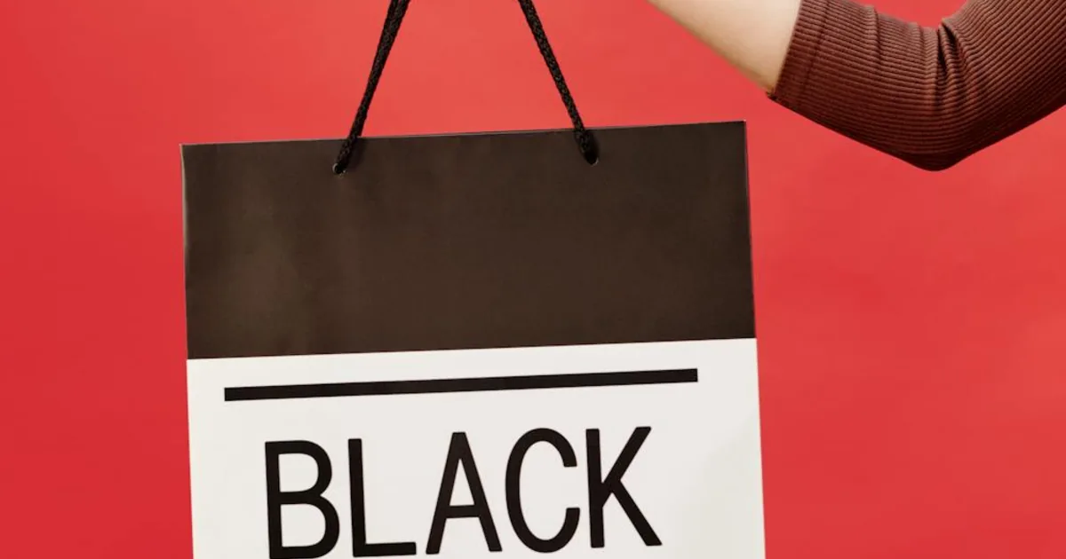 Hand holding a Black Friday shopping bag on red background — Shopify BFCM 2025 preparation guide for merchants